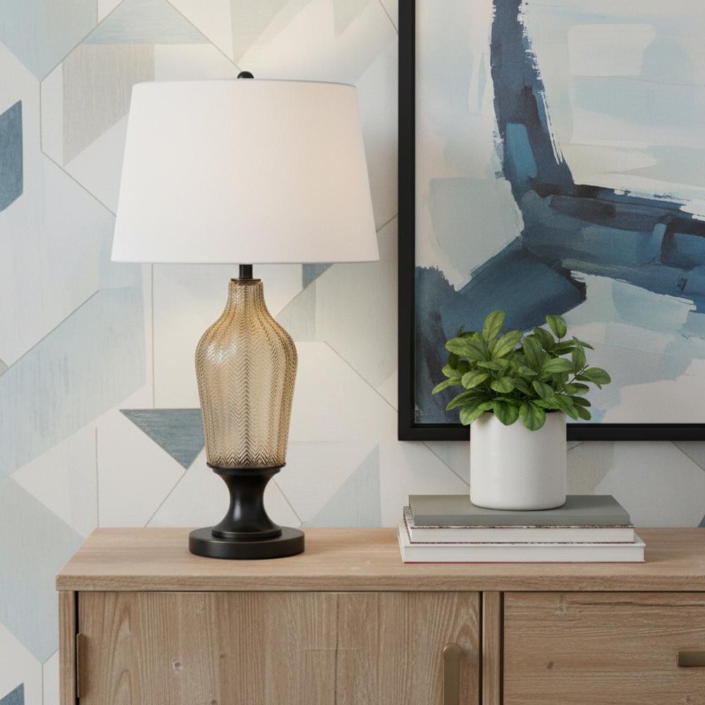 31" Bronze Glass Table Lamp With White Empire Shade displayed on a wood tabletop in a furnished interior against a light gray wall.