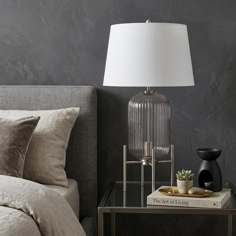 33" Nickel Glass Round Table Lamp With White Empire Shade displayed on a tabletop in a furnished interior against a dark wall in silver glass.