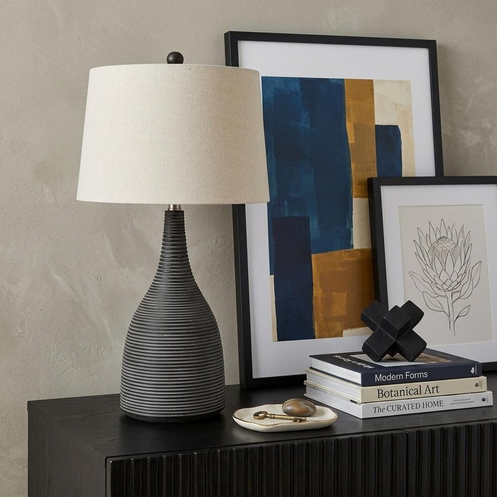 29" Black Ceramic Round Table Lamp With Beige Empire Shade displayed on a tabletop in a furnished interior against a tan wall.