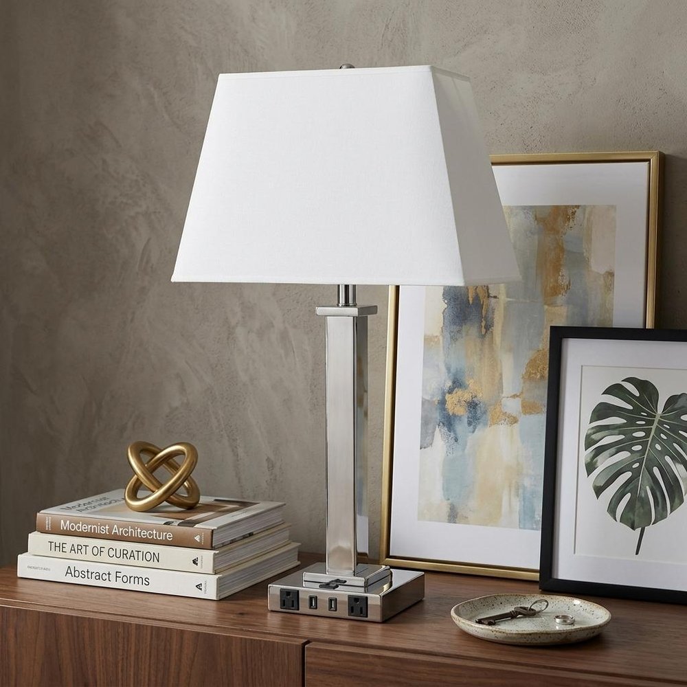 28" Nickel Metal USB Table Lamp With White Shade displayed on a dark wood tabletop in a furnished interior against a tan wall in silver metal.
