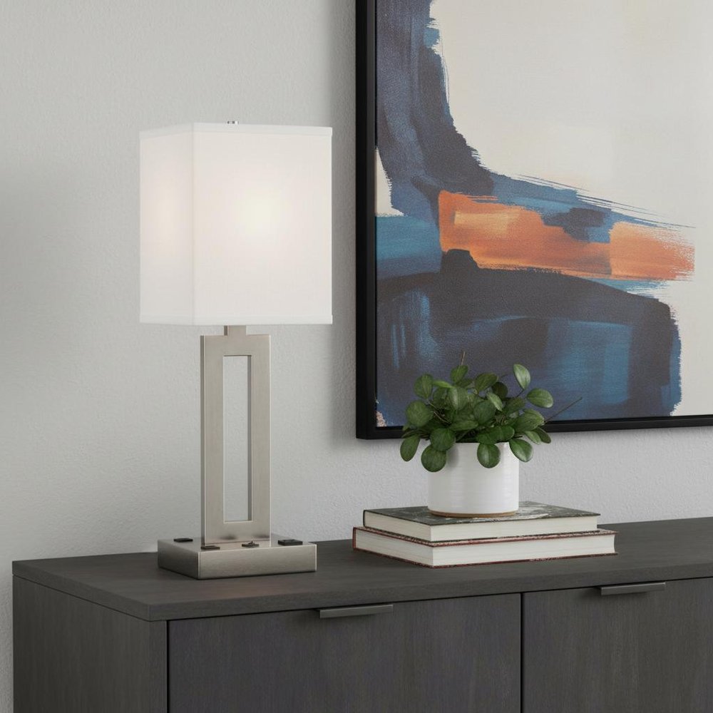 24" Nickel Metal Desk Usb Table Lamp With White Drum Shade displayed on a tabletop in a furnished interior against a light gray wall in silver metal.