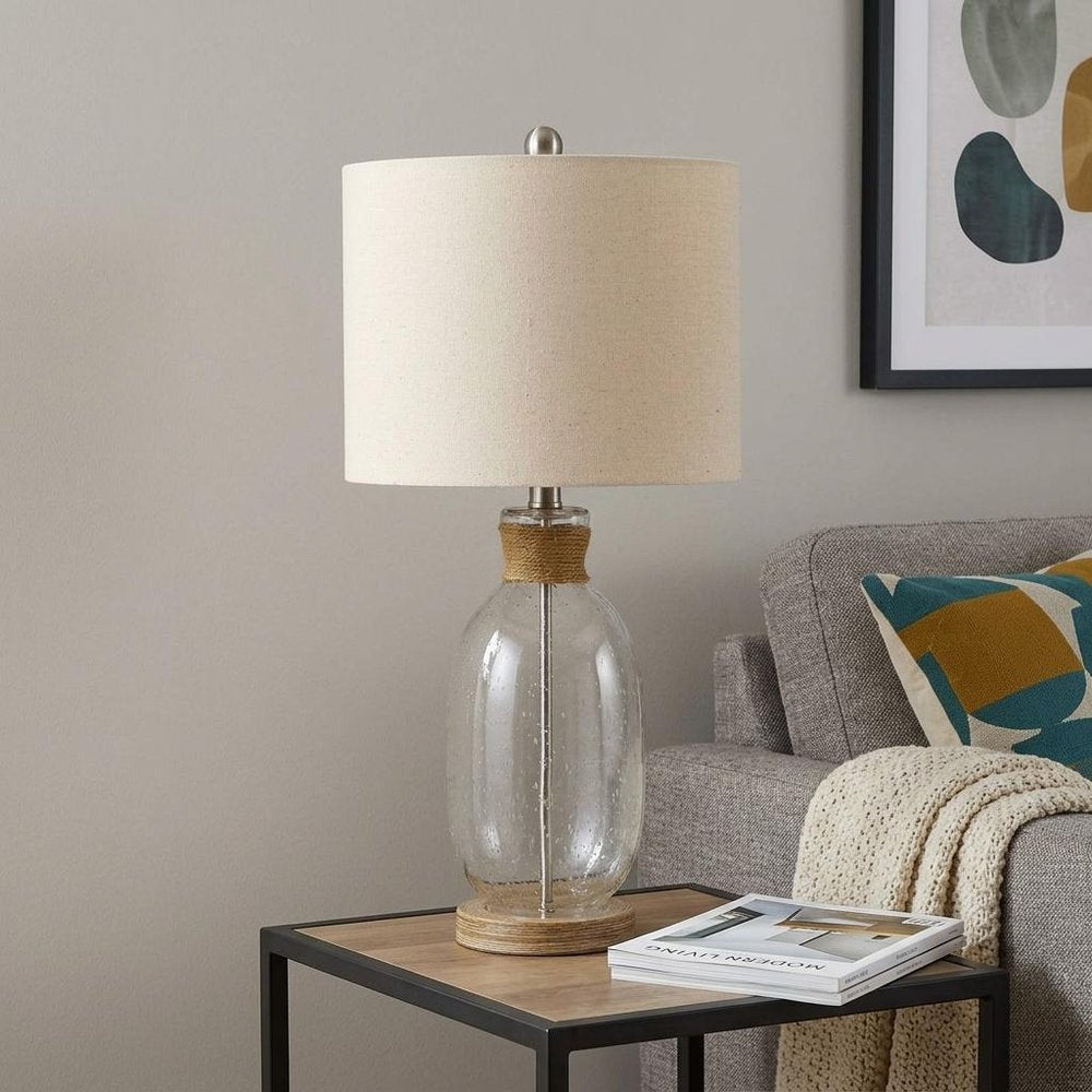 26" Brown Mason Jar Table Lamp With Brown Drum Shade displayed on a wood tabletop in a furnished interior against a light gray wall.
