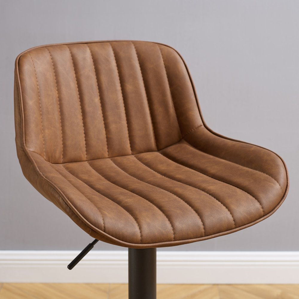 Brown faux leather low back adjustable height swivel bar chair with a black base against a gray wall and wooden floor.