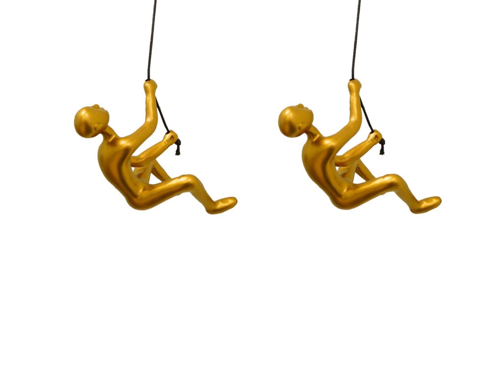 Two gold resin climbing man sculptures hanging from black ropes against a white background.
