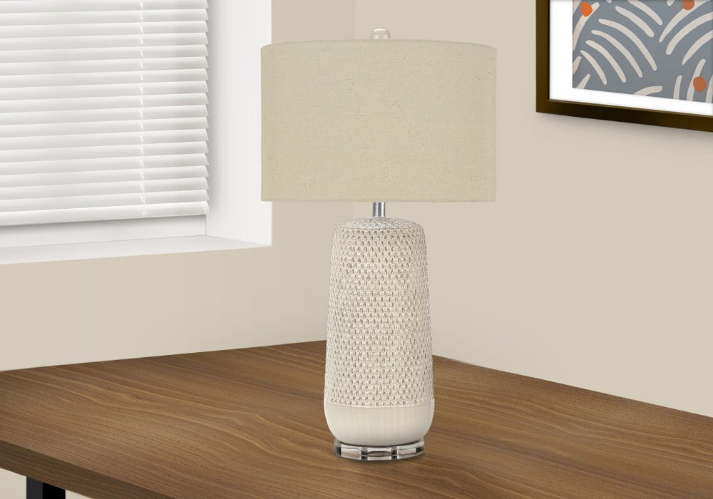 31" Cream Ceramic Geometric Table Lamp With Beige Drum Shade displayed on a wood tabletop in a furnished interior against a cream wall.