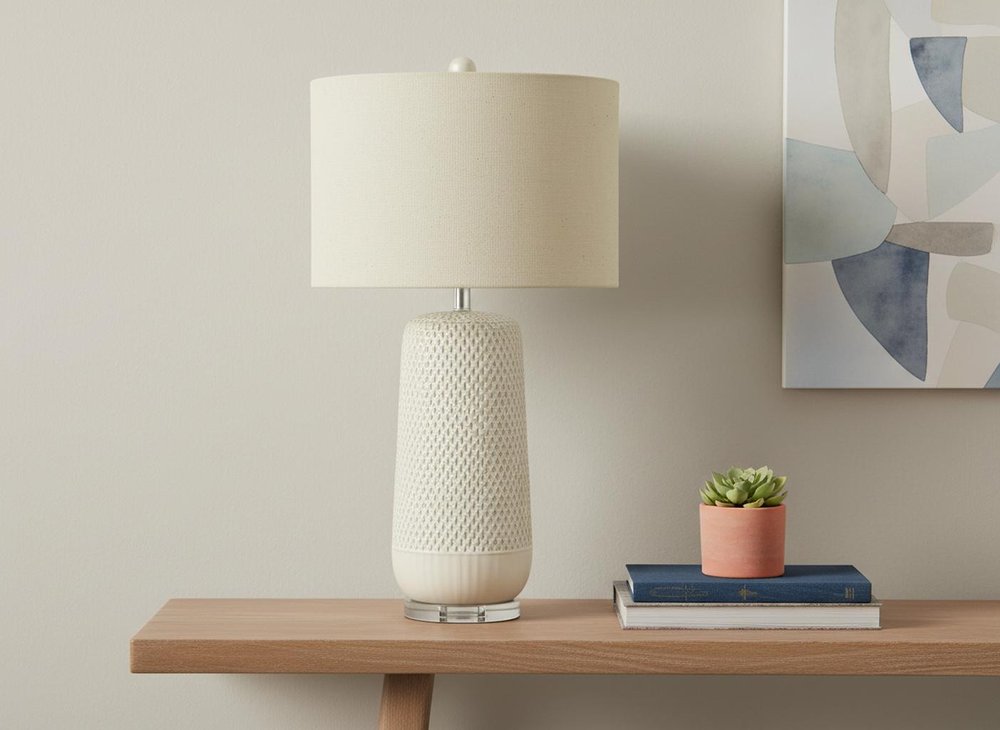 31" Cream Ceramic Geometric Table Lamp With Beige Drum Shade displayed on a dark wood tabletop in a furnished interior against a light gray wall.