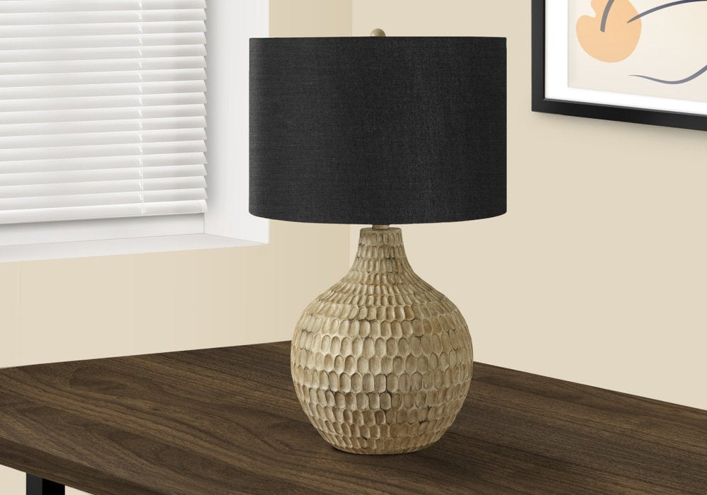25" Brown Geometric Table Lamp With Black Drum Shade displayed on a dark wood tabletop in a furnished interior against an off-white wall.