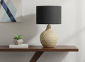 25" Brown Geometric Table Lamp With Black Drum Shade displayed on a tabletop in a furnished interior against an off-white wall.