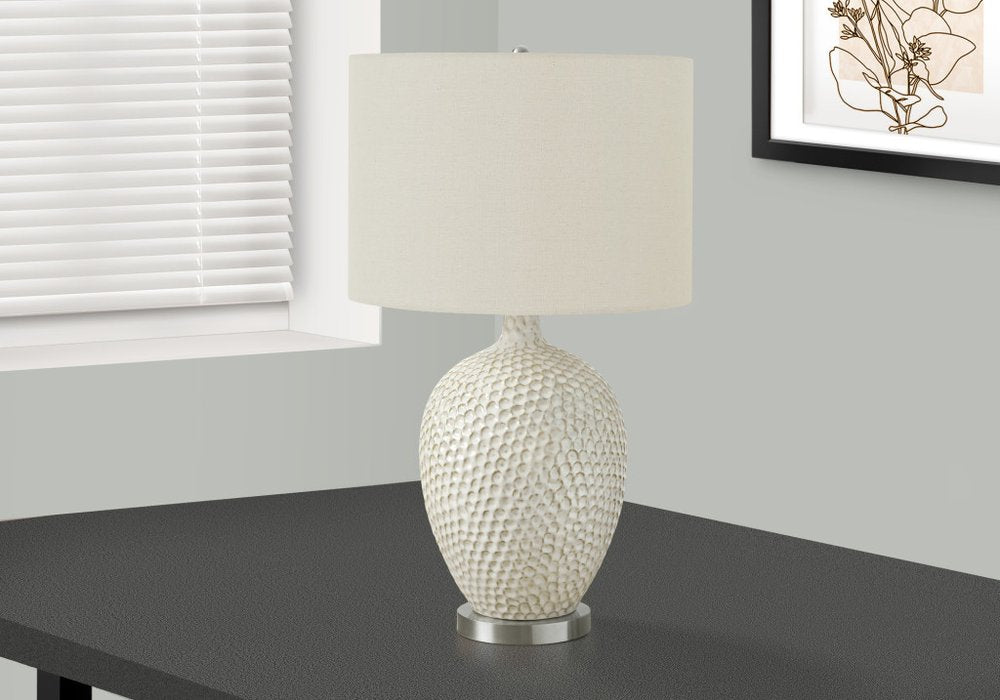 28" White and Silver Ceramic Round Table Lamp With Cream Drum Shade displayed on a tabletop in a furnished interior against an off-white wall.