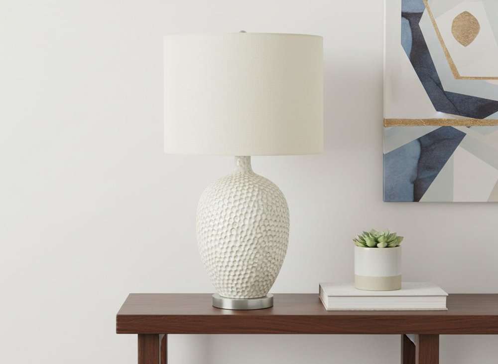 28" White and Silver Ceramic Round Table Lamp With Cream Drum Shade displayed on a tabletop in a furnished interior against an off-white wall.