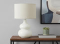 25" Cream Ceramic Gourd Table Lamp With Cream Drum Shade displayed on a dark wood tabletop in a furnished interior against a light gray wall.
