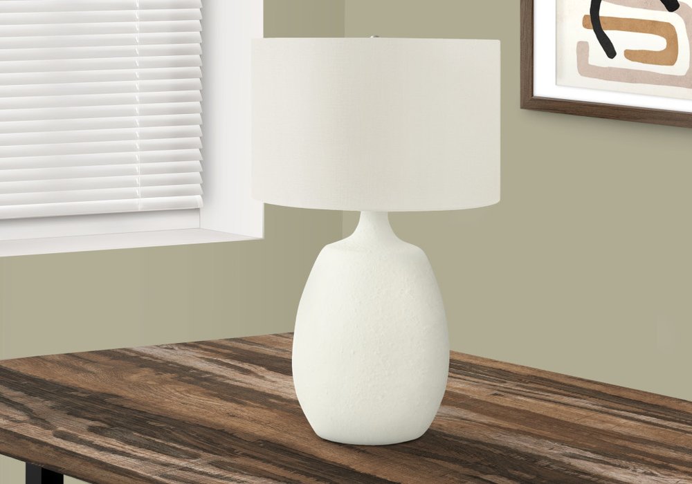 26" Cream Gourd Table Lamp With Cream Drum Shade displayed on a dark wood tabletop in a furnished interior against an off-white wall.