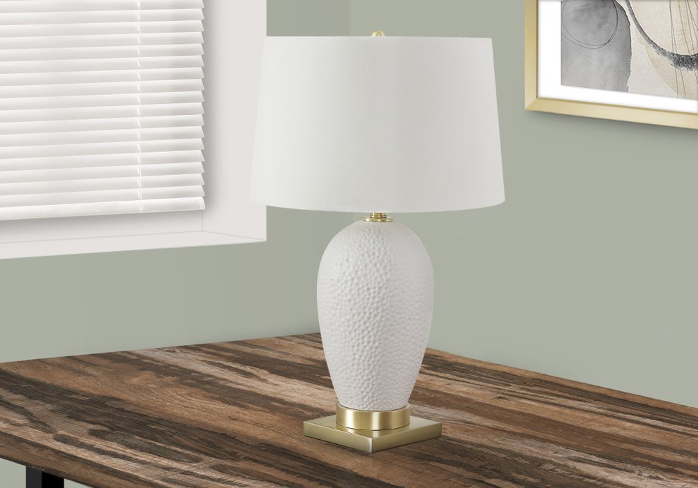 26" Gold and White Ceramic Urn Table Lamp With Cream Empire Shade displayed on a dark wood tabletop in a furnished interior against an off-white wall.