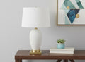 26" Gold and White Ceramic Urn Table Lamp With Cream Empire Shade displayed on a dark wood tabletop in a furnished interior against an off-white wall.