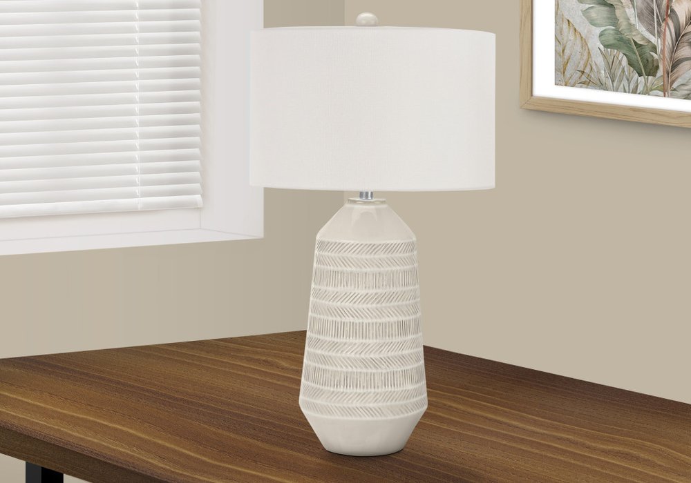 33" Ivory Ceramic Geometric Table Lamp With Cream Drum Shade displayed on a dark wood tabletop in a furnished interior against an off-white wall.