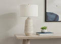 33" Ivory Ceramic Geometric Table Lamp With Cream Drum Shade displayed on a wood tabletop in a furnished interior against a light gray wall.