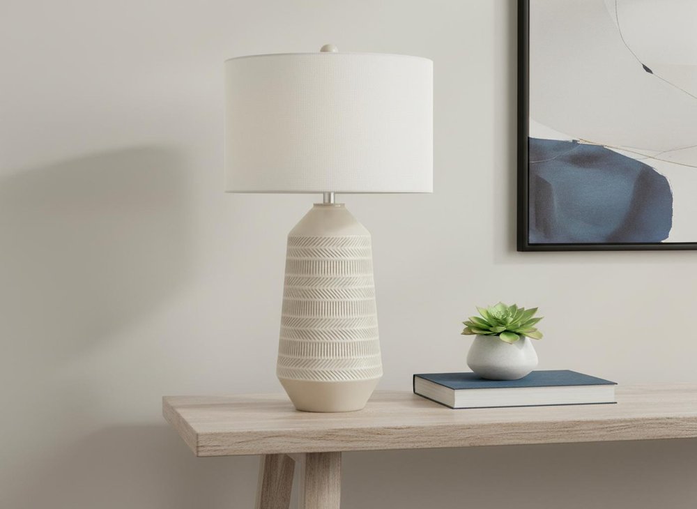 33" Ivory Ceramic Geometric Table Lamp With Cream Drum Shade displayed on a wood tabletop in a furnished interior against a light gray wall.