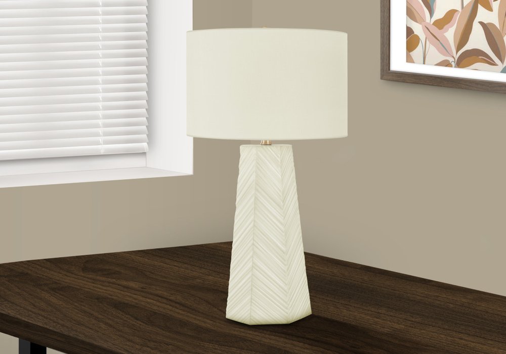 29" White Ceramic Geometric Table Lamp With Ivory Drum Shade displayed on a dark wood tabletop in a furnished interior against an off-white wall.