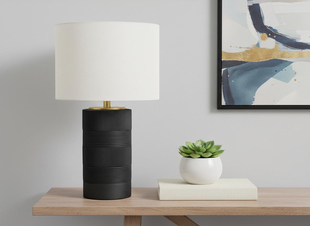 24" Black Cylinder Table Lamp With Ivory Drum Shade displayed on a wood tabletop in a furnished interior against an off-white wall.