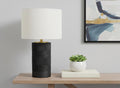 24" Black Cylinder Table Lamp With Ivory Drum Shade displayed on a wood tabletop in a furnished interior against an off-white wall.