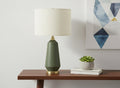 26" Green Ceramic Geometric Table Lamp With Ivory Drum Shade displayed on a dark wood tabletop in a furnished interior against an off-white wall.
