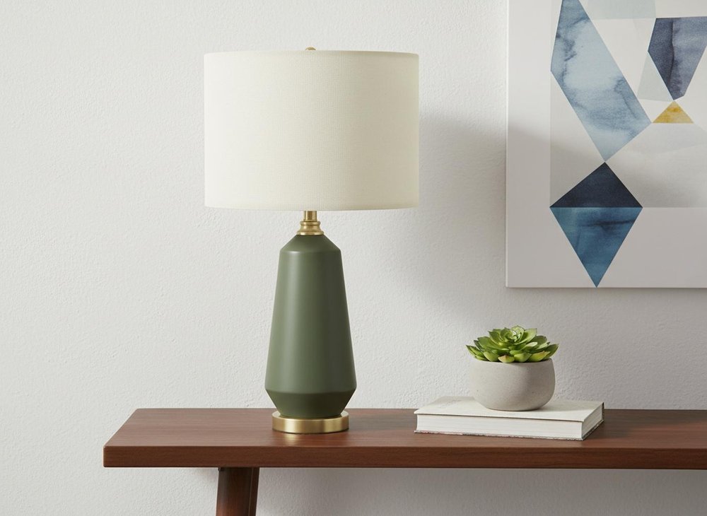 26" Green Ceramic Geometric Table Lamp With Ivory Drum Shade displayed on a dark wood tabletop in a furnished interior against an off-white wall.