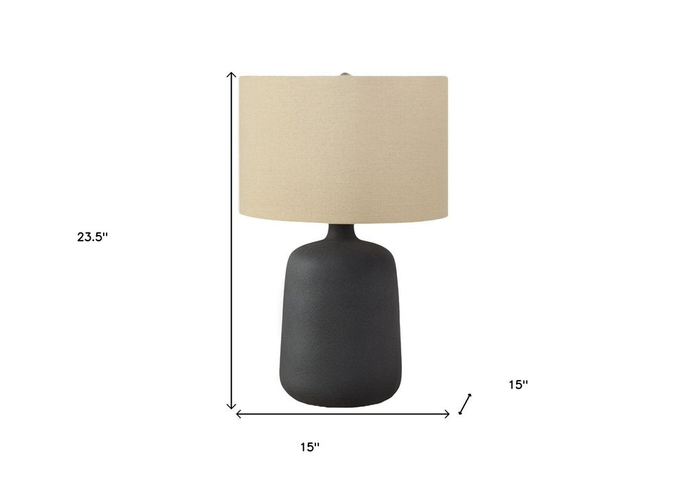 24" Black Ceramic Round Table Lamp With Beige Drum Shade. Table lamp isolated on a plain white background, in a beige ceramic finish.