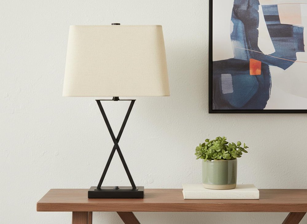 25" Black Metal Geometric USB Table Lamp With Beige Shade displayed on a wood tabletop in a furnished interior against an off-white wall.
