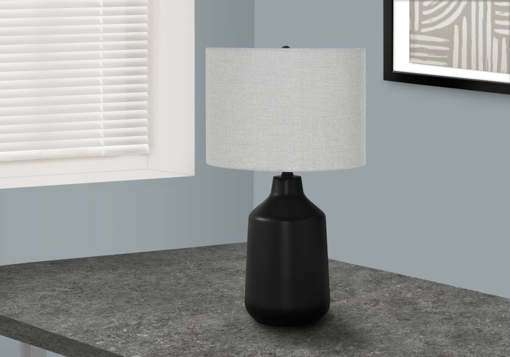 24" Black Concrete Urn Table Lamp With Gray Drum Shade displayed on a tabletop in a furnished interior against an off-white wall.