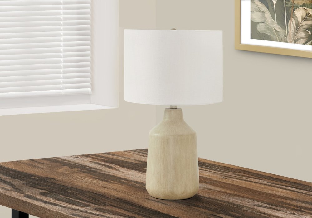 24" Beige Concrete Urn Table Lamp With Ivory Drum Shade displayed on a dark wood tabletop in a furnished interior against an off-white wall.