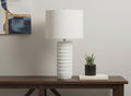28" Cream Cylinder Table Lamp With Cream Drum Shade displayed on a dark wood tabletop in a furnished interior against an off-white wall.