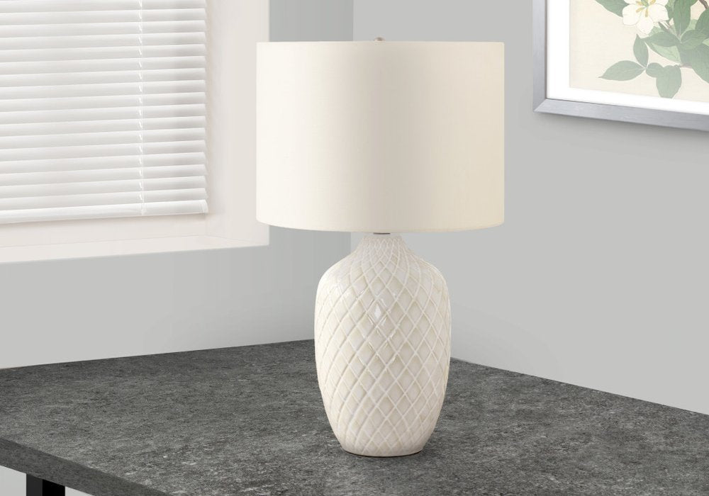 25" Cream Ceramic Urn Table Lamp With Cream Drum Shade displayed on a tabletop in a furnished interior against an off-white wall.