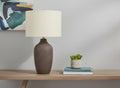 27" Gray Ceramic Urn Table Lamp With Beige Drum Shade displayed on a tabletop in a furnished interior against a light gray wall.