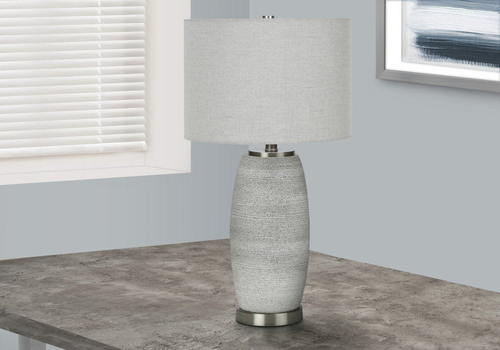 25" Gray and Silver Ceramic Cylinder Table Lamp With Gray Drum Shade displayed on a tabletop in a furnished interior against an off-white wall.