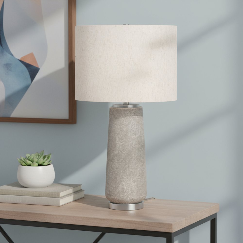 29" Gray and Silver Cylinder Table Lamp With Ivory Drum Shade displayed on a wood tabletop in a furnished interior against a light gray wall.