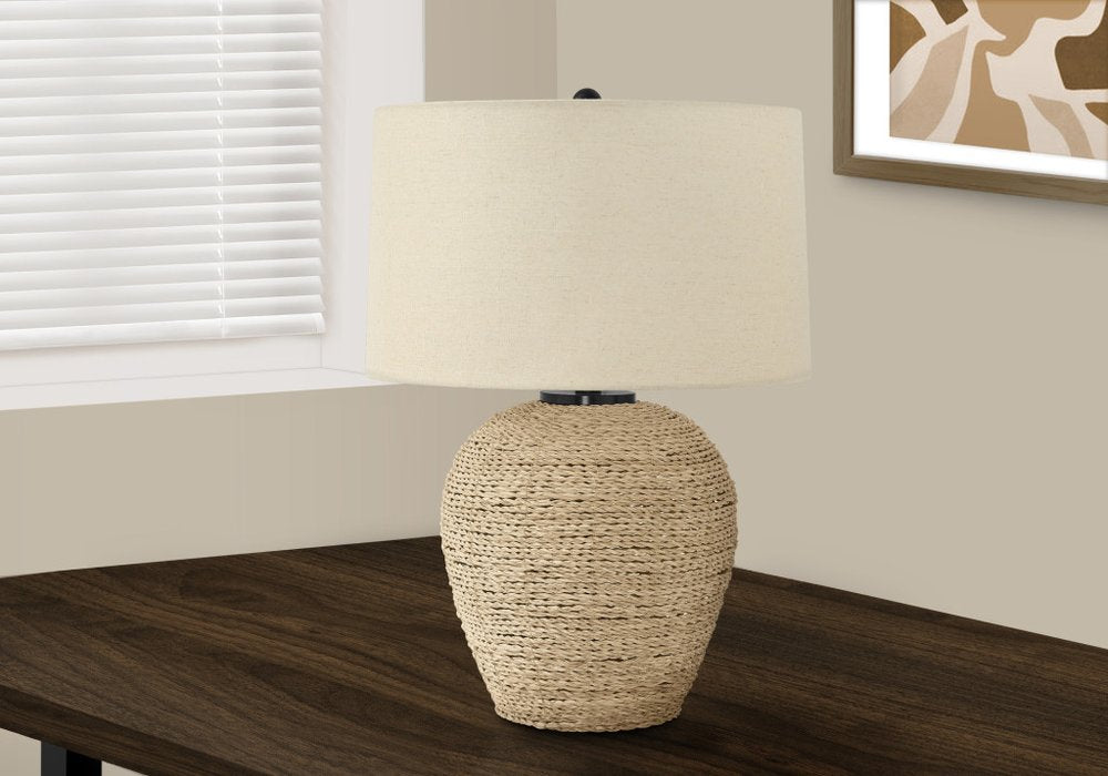 25" Beige Rattan Round Table Lamp With Beige Drum Shade displayed on a dark wood tabletop in a furnished interior against an off-white wall.