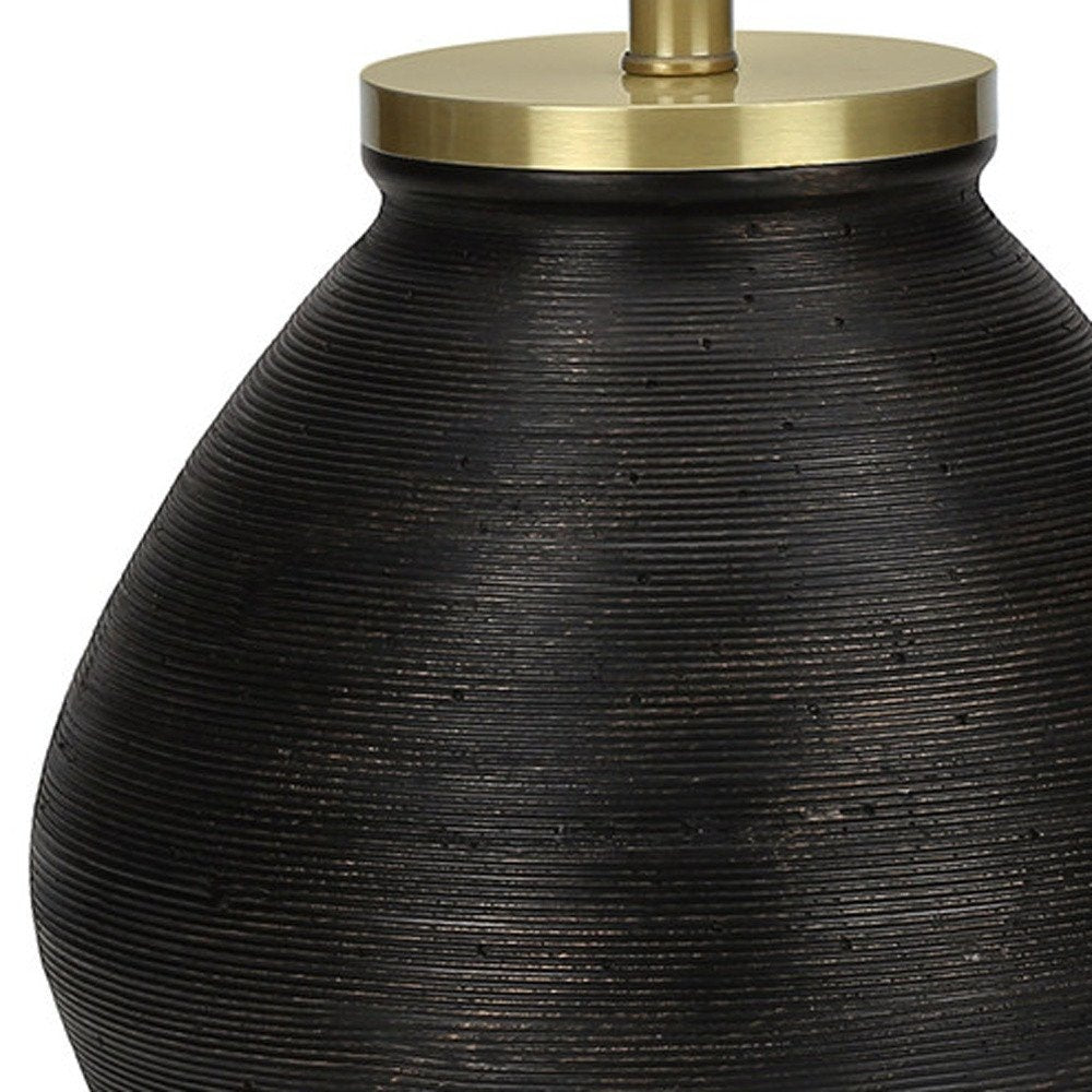 25" Black and Gold Concrete Round Table Lamp With Ivory Drum Shade photographed against a dark studio background in gold.