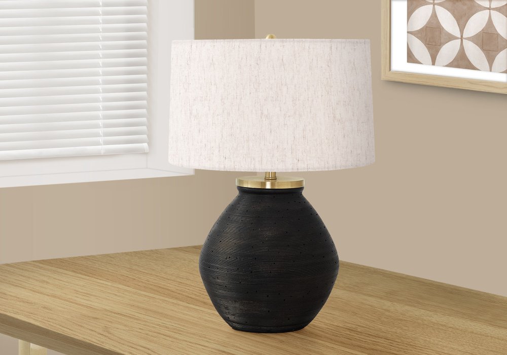 25" Black and Gold Concrete Round Table Lamp With Ivory Drum Shade displayed on a wood tabletop in a furnished interior against an off-white wall.