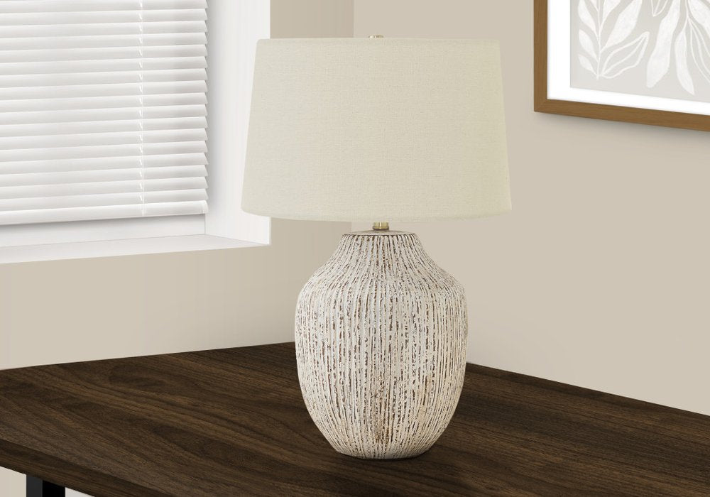 26" Cream Ceramic Round Table Lamp With Cream Empire Shade displayed on a dark wood tabletop in a furnished interior against an off-white wall.