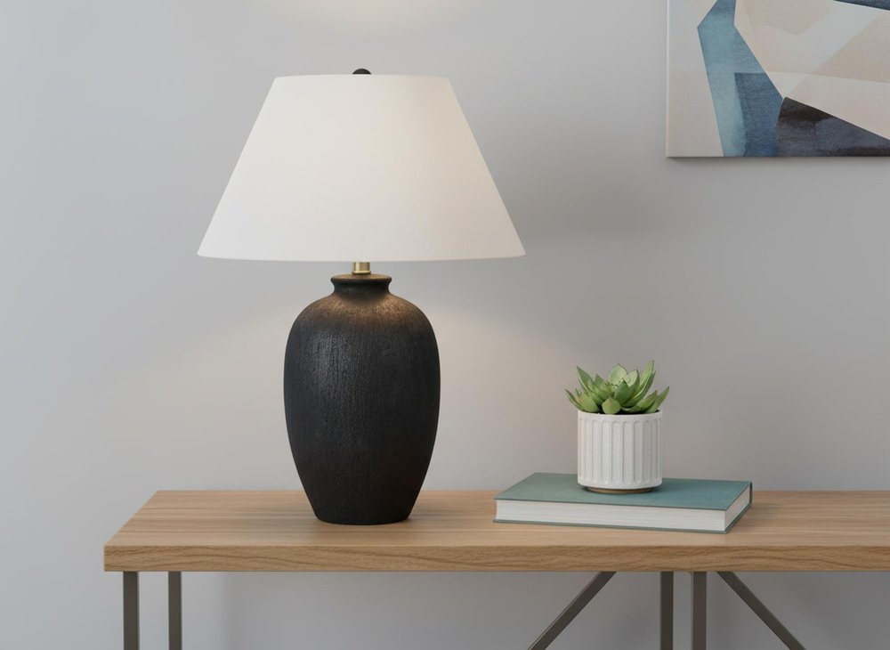 24" Black Ceramic Round Table Lamp With Ivory Empire Shade displayed on a tabletop in a furnished interior against a light gray wall.