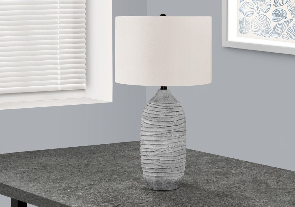 27" Gray Cylinder Table Lamp With Ivory Drum Shade displayed on a tabletop in a furnished interior against an off-white wall.