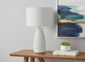27" Gray and White Ceramic Round Table Lamp With Gray Drum Shade displayed on a wood tabletop in a furnished interior against an off-white wall.