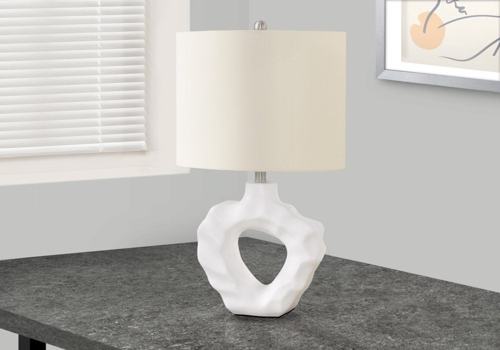 25" Cream Novelty Table Lamp With Cream Drum Shade displayed on a tabletop in a furnished interior against an off-white wall.