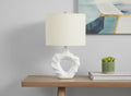 25" Cream Novelty Table Lamp With Cream Drum Shade displayed on a tabletop in a furnished interior against a light gray wall.