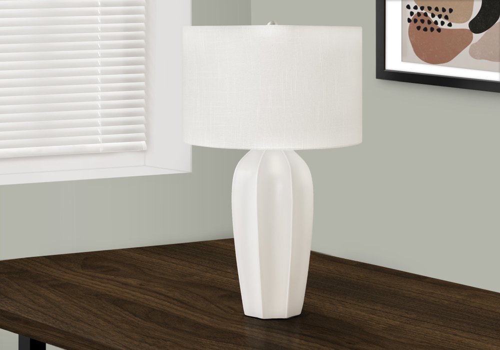 27" Cream Ceramic Geometric Table Lamp With Cream Drum Shade displayed on a dark wood tabletop in a furnished interior against an off-white wall.