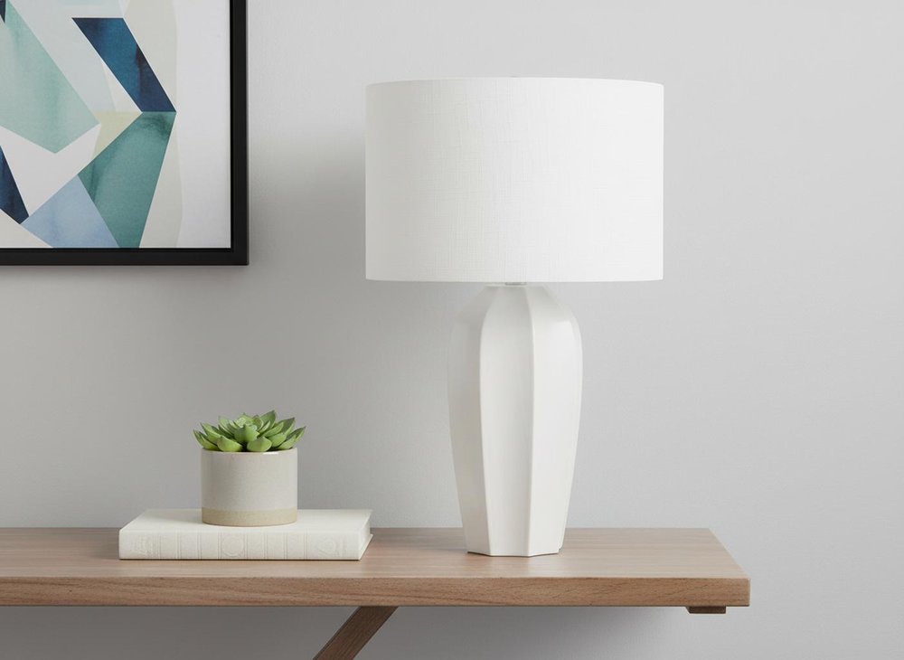 27" Cream Ceramic Geometric Table Lamp With Cream Drum Shade displayed on a tabletop in a furnished interior against an off-white wall.