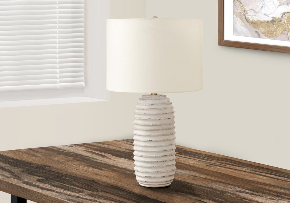 28" Cream Geometric Table Lamp With Cream Drum Shade displayed on a dark wood tabletop in a furnished interior against an off-white wall.