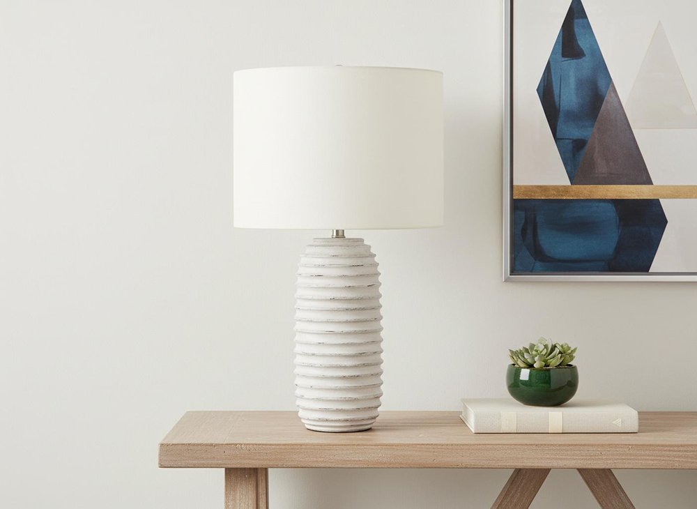 28" Cream Geometric Table Lamp With Cream Drum Shade displayed on a wood tabletop in a furnished interior against an off-white wall.