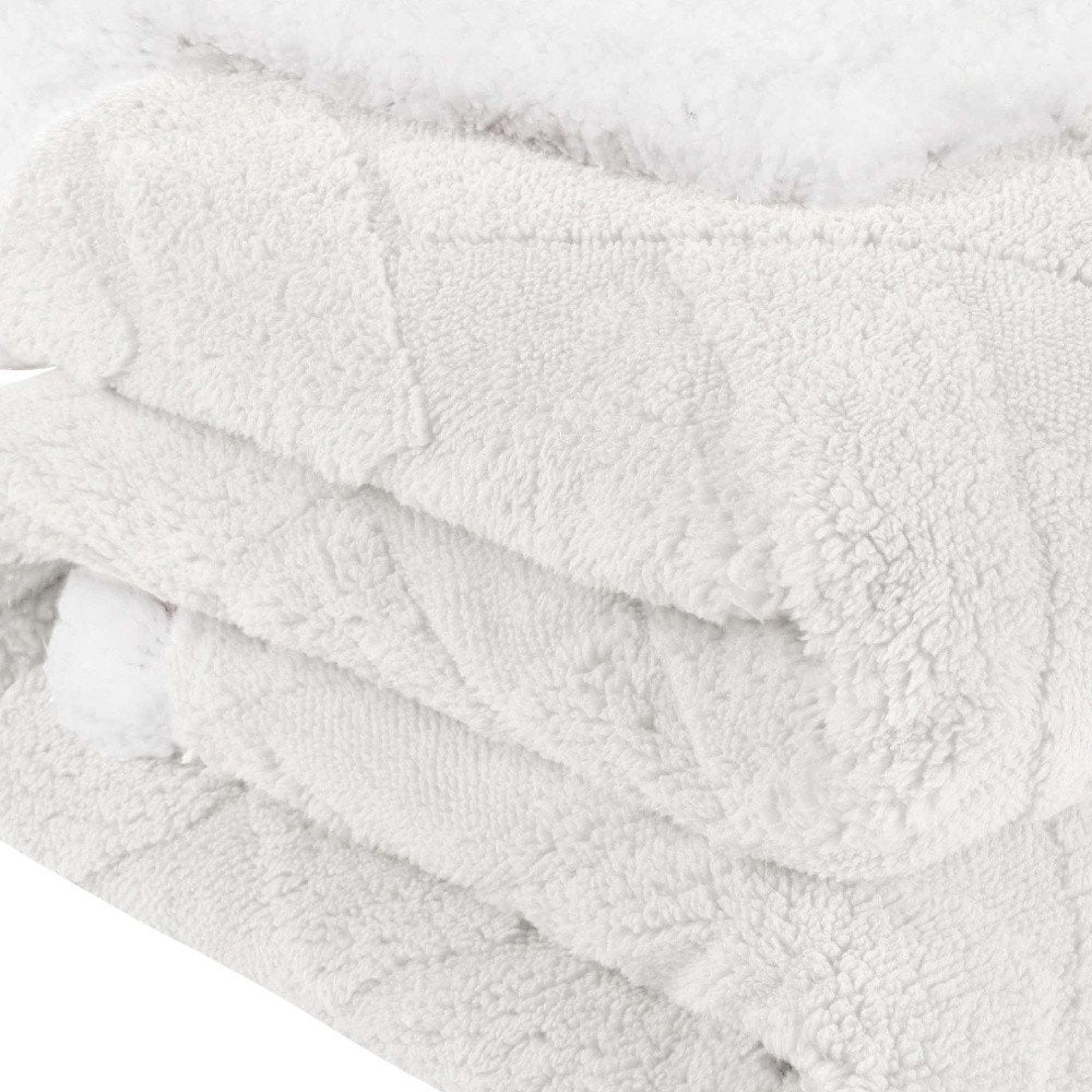 Close-up of a folded white fleece knitted plush blanket with a textured surface and a fluffy edge.