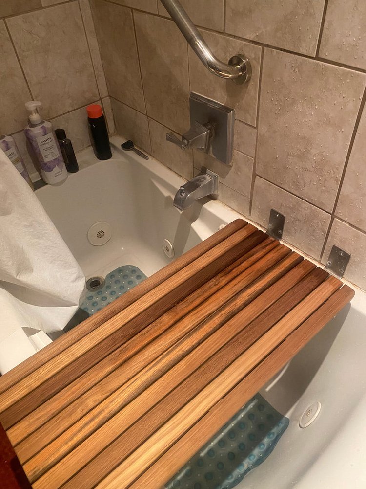 Brown teak shower bench mounted on a tiled bathroom wall above a bathtub.